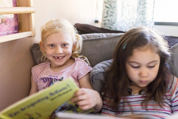 Två förskolebarn sitter tillsammans i en soffa och läser.