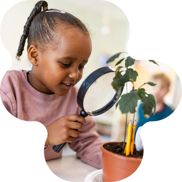 Barn på förskolan tittar på planta genom förstoringsglas.